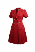 Robe blazer rouge Anthiope avec jupe plissée, double boutonnage doré et ceinture fine en chaîne, portée par une femme